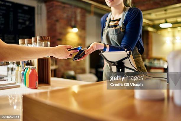 Female barista taking smartphone contactless payment from coffee shop customer