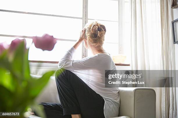 woman sitting in front of window looking out - woman worried bildbanksfoton och bilder
