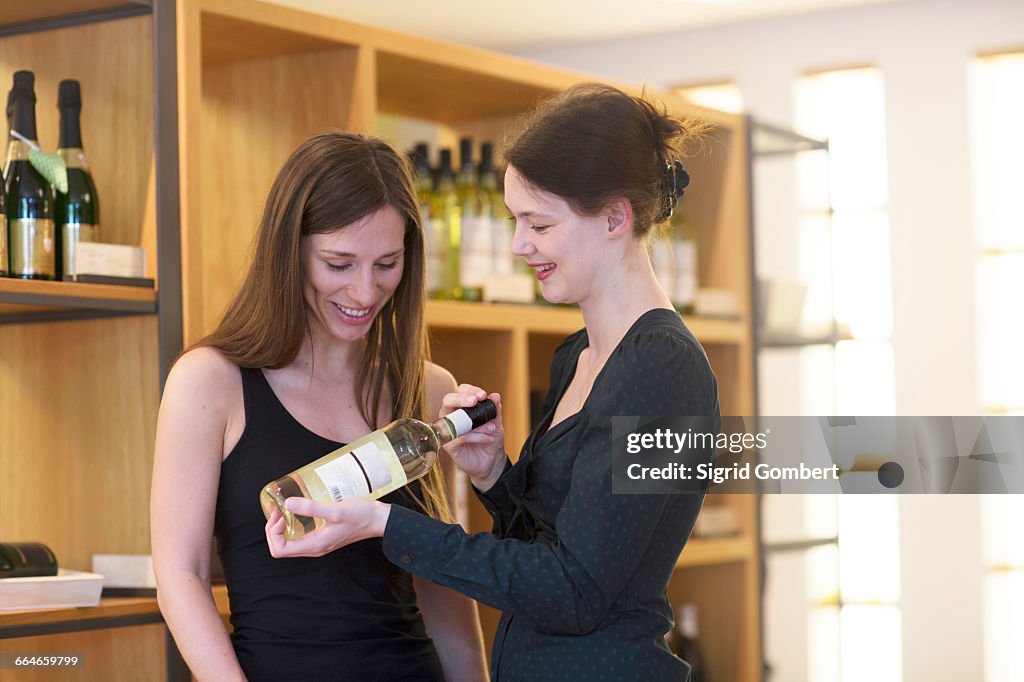 Sales assistant in wine shop recommending bottle of wine to customer