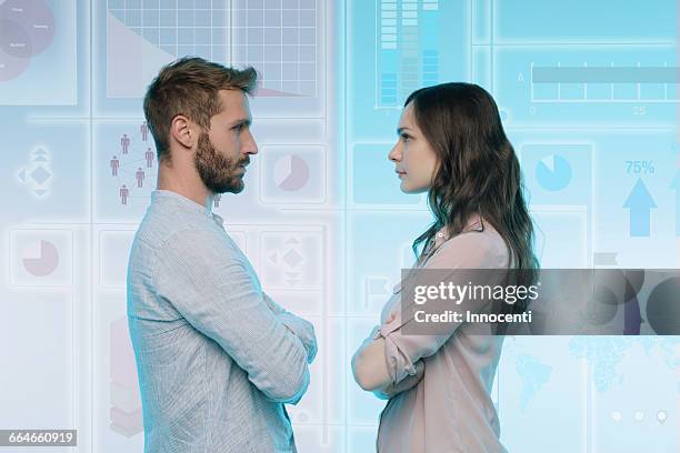 man and woman standing face to face, data on graphical screen behind them - confrontation photos et images de collection