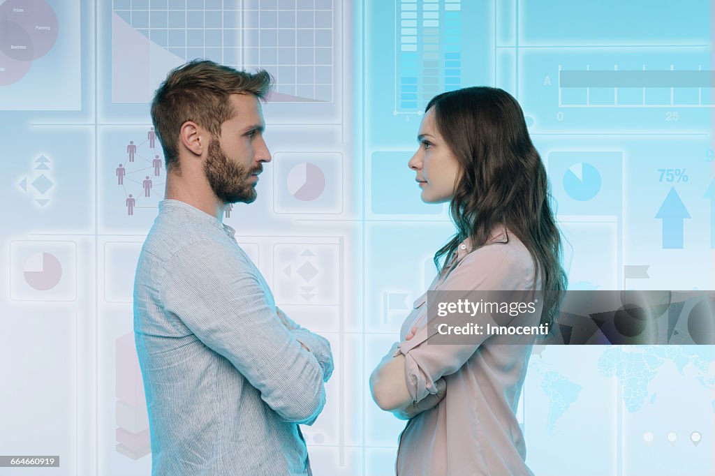 Man and woman standing face to face, data on graphical screen behind them