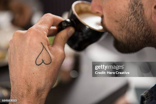 cropped view of tattooed man drinking coffee - coffee heart fotografías e imágenes de stock