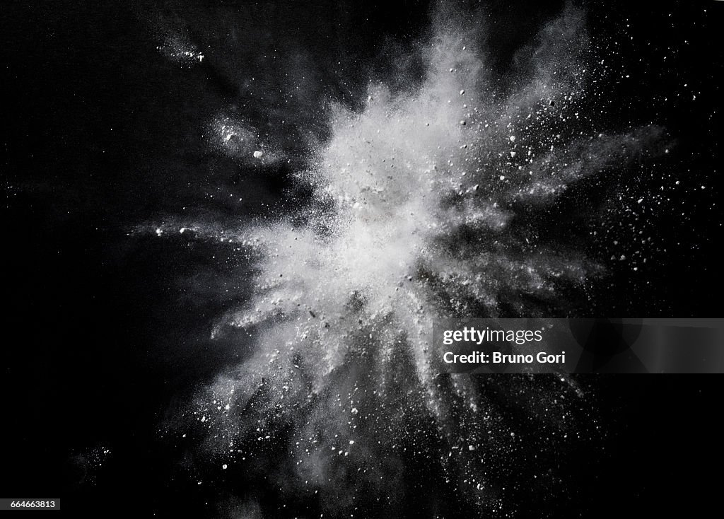 White dust exploding mid air against black background