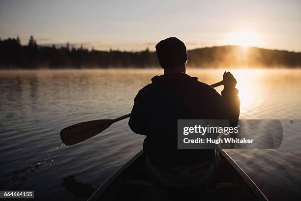 senior man canoeing on lake at sunset, rear view - seniors canoeing stock pictures, royalty-free photos & images