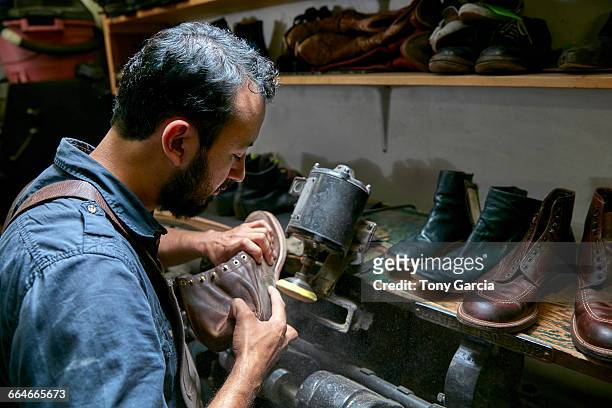 male cobbler in traditional shoe workshop inspecting boot - shoe repair stockfoto's en -beelden