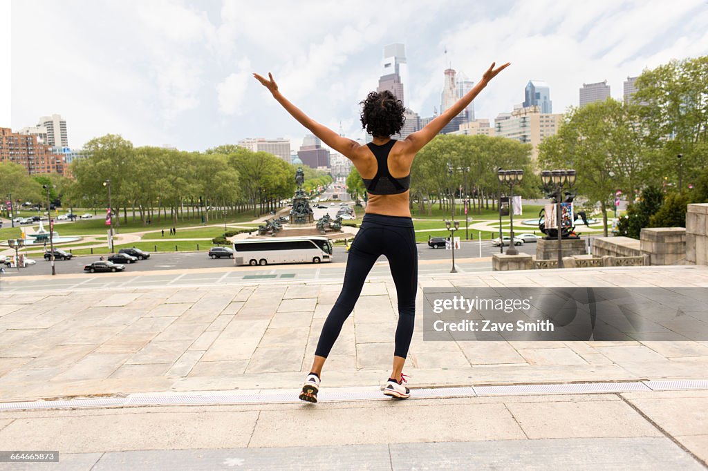 Rear view of woman wearing sports clothing, arms raised looking at city