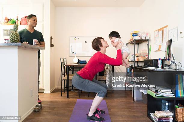 Father watching mother doing squats with baby in arms