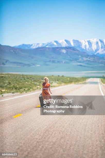 young 1950s style woman walking alone on highway 50 pulling wheeled suitcase, nevada, usa - s incredible women of 2016 stock pictures, royalty-free photos & images