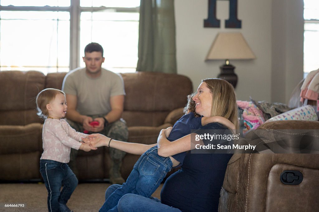 Male soldier and wife playing with daughters in living room at air force military base