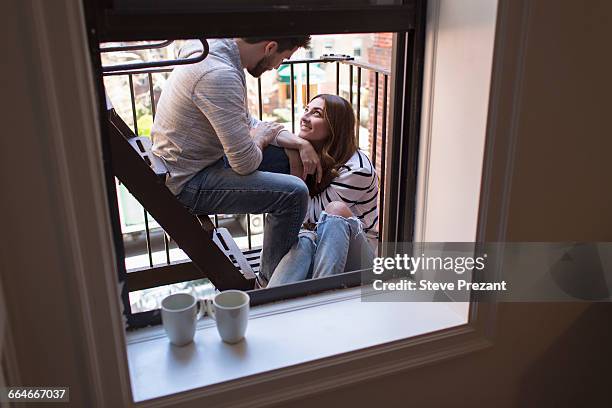 young couple sitting on fire escape, smiling - fire escape stock pictures, royalty-free photos & images