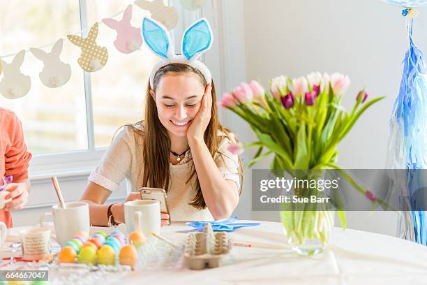 teenage girl at table reading smartphone texts whilst dyeing hard boiled eggs for easter - kid boiled egg stock pictures, royalty-free photos & images