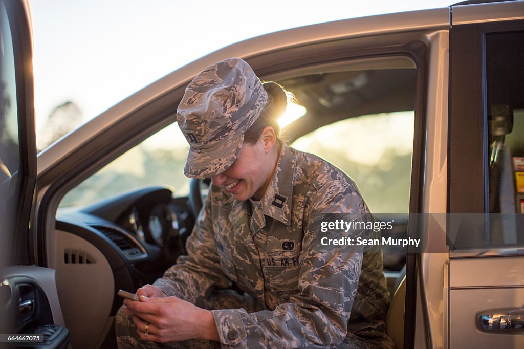 Female soldier sitting in car texting on smartphone at air force military base