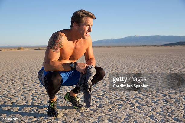 man training crouching bare chested on dry lake bed, el mirage, california, usa - el mirage photos et images de collection