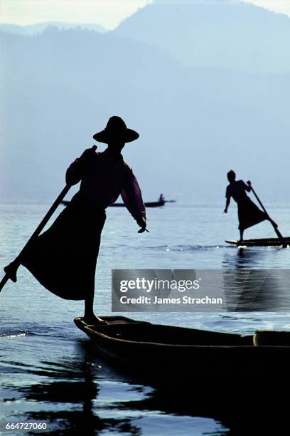 silhouetted leg-rowers, inle lake, myanmar - cheroot stock-fotos und bilder