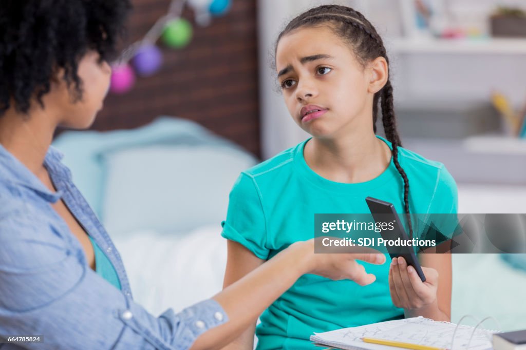 Tween girl hands her phone over to her mother
