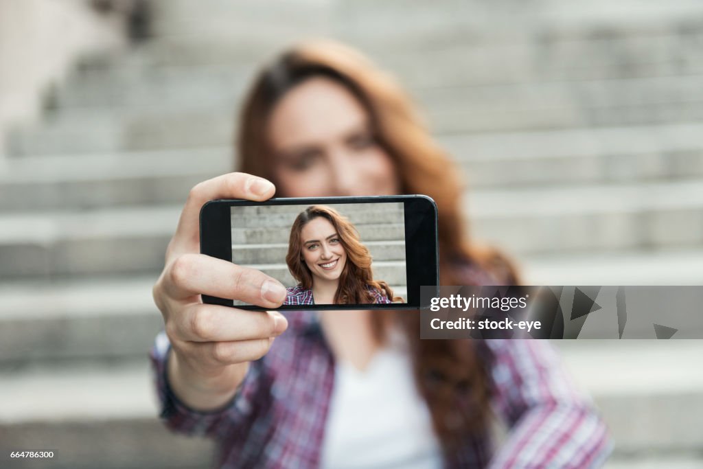 Beautiful woman makes self portrait on smartphone view of screen
