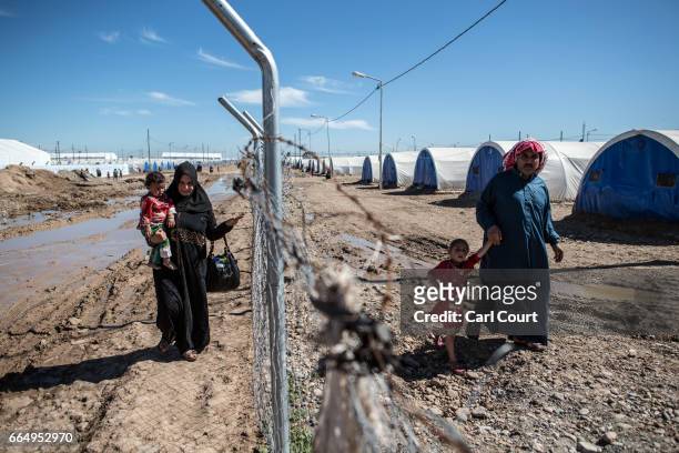 Woman carrying a child and a man holding the hand of another child all make their way along a fence in Hamam al-Alil refugee camp where large numbers...
