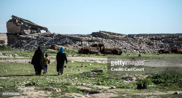 Women and a child walk past the ruins of a building destroyed by fighting near Hamam al-Alil refugee camp where large numbers of people have settled...