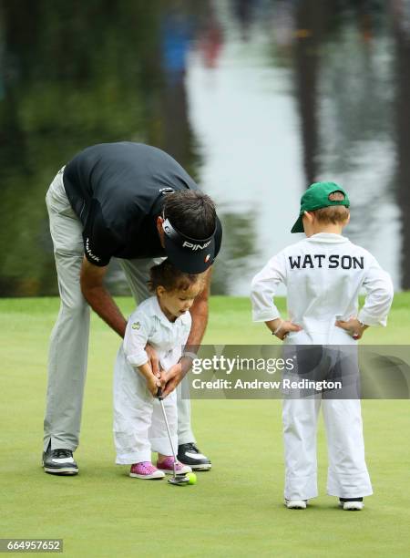 Bubba Watson of the United States helps his daughter Dakota putt as son Caleb looks on during the Par 3 Contest prior to the start of the 2017...