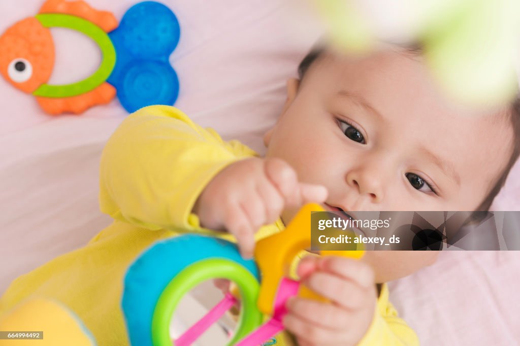 Happy Baby lag in seinem Bettchen Spielzeug aufmerksam betrachten