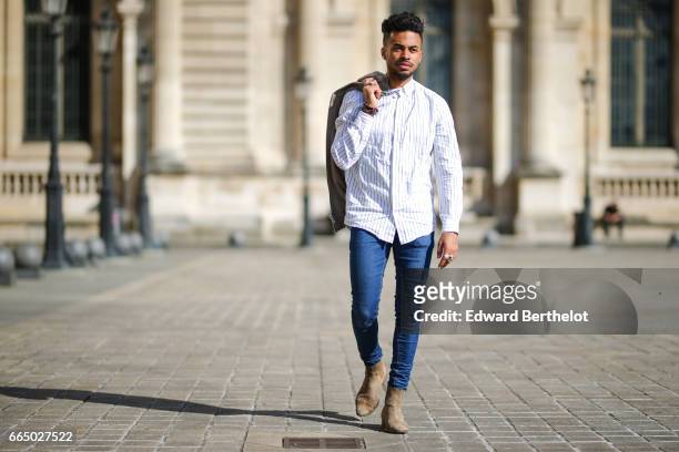 Theo Kimbaloula, fashion blogger, wears a Wac beige jacket, a Wac shirt, Asos blue jeans, and The Kooples beige suede boots, at the Louvre, on April...