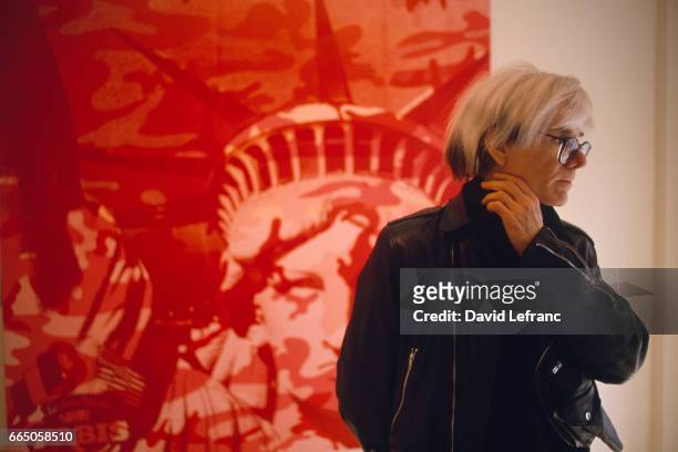 American Painter Andy Warhol, standing in front of a painting, circa 1970.