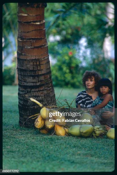 Marlene Jobert sits by coconuts and holds a child while on vacation in Mauritius.