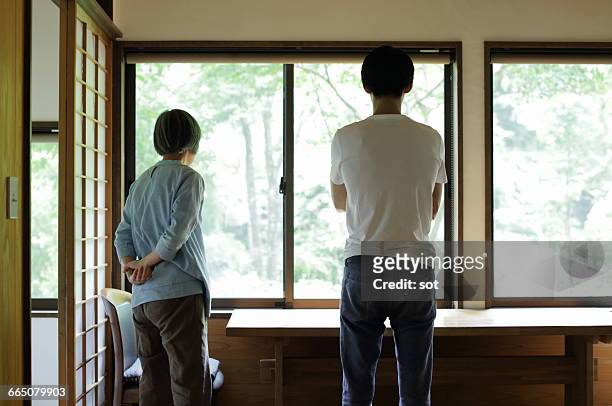 son and mother looking out of window,rear view - hands behind back stock photos et images de collection