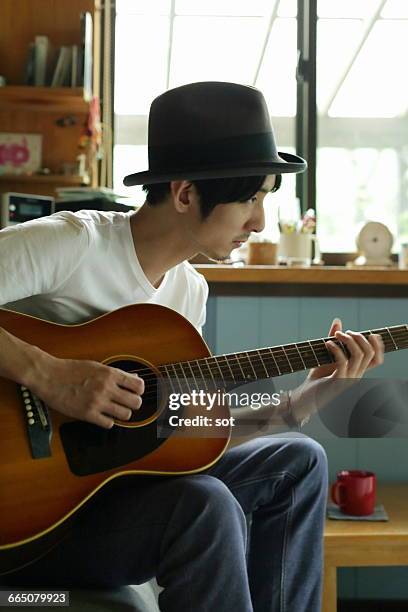 young man playing guitar in living room - man fedora room stock pictures, royalty-free photos & images