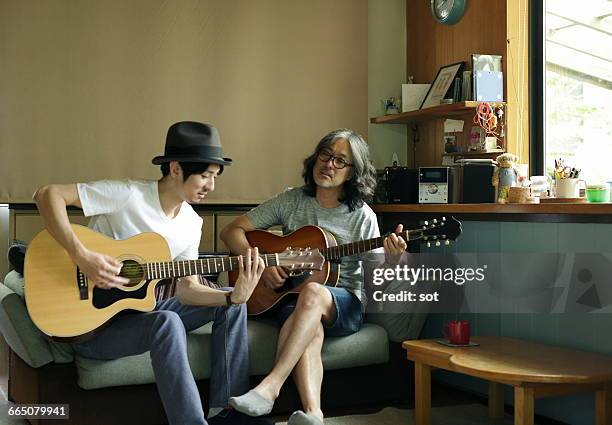 two men playing guitar on sofa in living room - man fedora room stock pictures, royalty-free photos & images