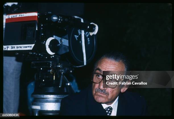 On the set of the movie "Cento Giorni a Palermo", directed by Giuseppe Ferrara, actor Lino Ventura, wearing a dark suit, a tie and a shirt, takes a...