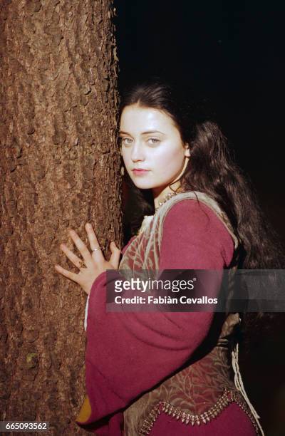 Young actress Monica Keena, playing Lilliana Hoffman and wearing an aristocrat's dress, poses with her hands around a tree at night time on the set...