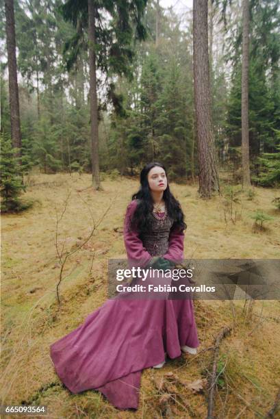 Young actress Monica Keena, playing Lilliana Hoffman and wearing an aristocrat's dress, sits in the middle of a forest with trees behind her on the...