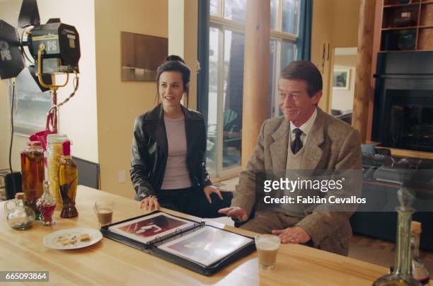 Actors Fiona Loewi and John Hurt sit together at a diner table, watching a picture book with coffee and cookies in front of them on the set of the...