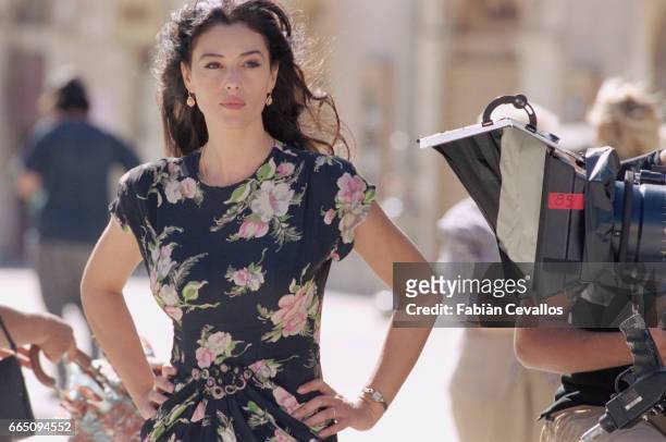 Italian actress Monica Bellucci, wearing a black dress with flowers, stands next to a camera with her hands on her hips on the set of the Italian...