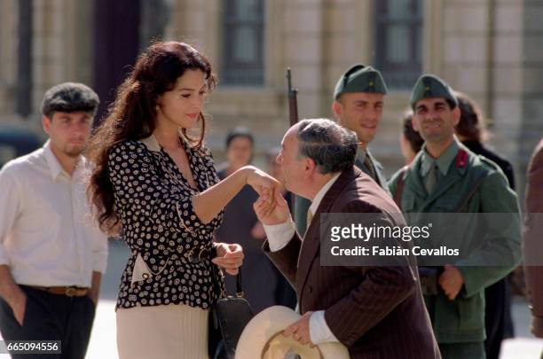 Man with his hat in his hand kisses Monica Bellucci's hand on a square with with two men in uniform and a passerby behind them in a scene taken from...