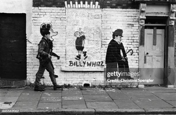Soldier walking down Falls Road in Belfast merges into a picture of Mickey Mouse on a wall next to drawings of cartoon character Billy Whizz and...