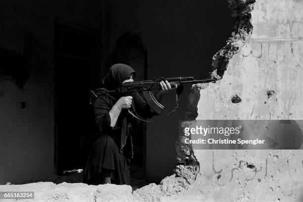 Woman aims an AK-47 rifle over a crumbling wall in West Beirut during the Lebanese Civil War.