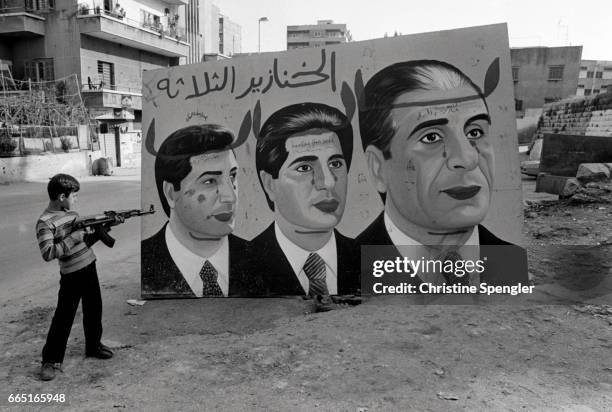 Lebanese boy points an assault rifle at a large mural of the Gemayel family, a family of Christian politicians prominent during the Lebanese Civil...