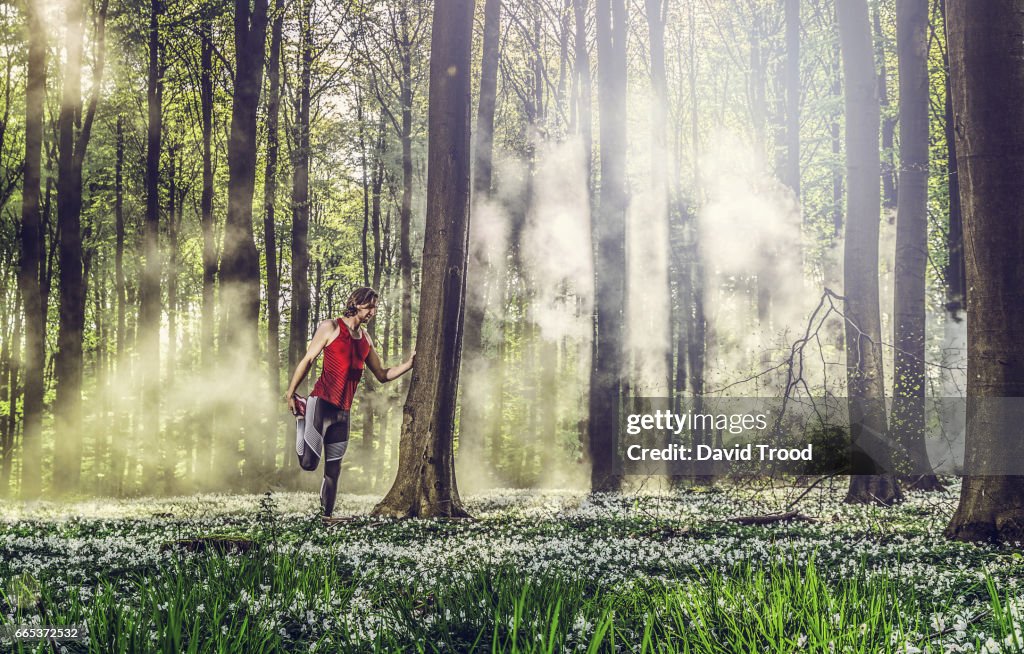 Male runner stretching before running in the forest.