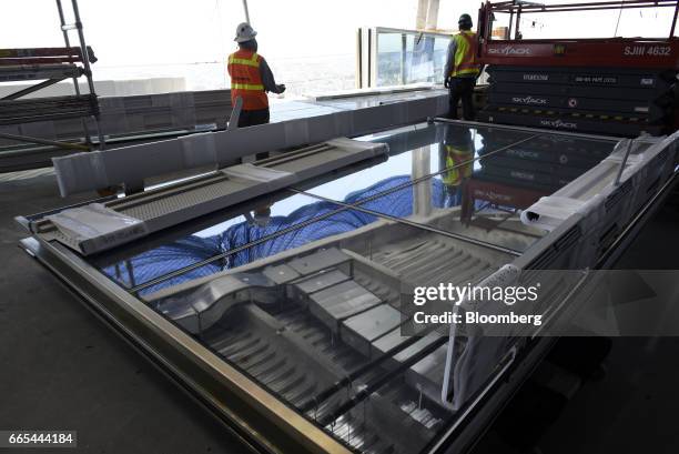 Contractors work near a section of glass curtain wall on the 61st floor of the Salesforce Tower as the Bay Bridge stands in San Francisco,...