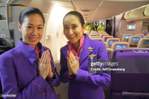 Two Asian women attendants greeting with hands clasped onboard the Thai Airways cabin at Frankfurt am Main Airport.