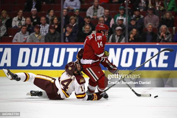 Alexander Kerfoot of the Harvard Crimson tries to get off a shot as he's grabbed by Alex Iafallo of the Minnesota-Duluth Bulldogs during game one of...