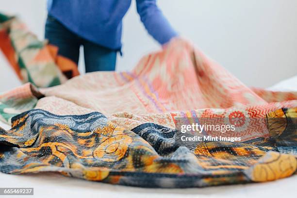 a woman spreading a fabric quilt over a bed in a bedroom. - duvet stock pictures, royalty-free photos & images