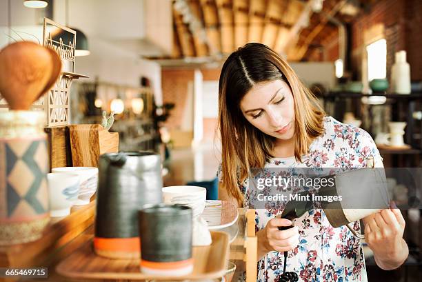 young woman in a shop, scanning the barcode of a ceramic jug with a barcode scanner. - scanner stock stock pictures, royalty-free photos & images