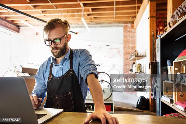 a man in a bicycle repair shop using a laptop computer. running a business. - computer store stockfoto's en -beelden