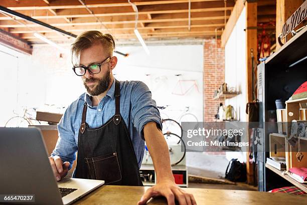 a man in a bicycle repair shop using a laptop computer. running a business. - small business laptop bildbanksfoton och bilder