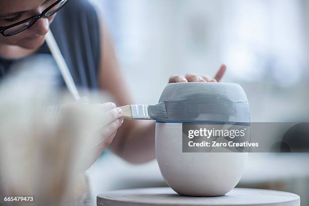 female potter painting ceramic glaze on vase in workshop - painting pottery stock pictures, royalty-free photos & images