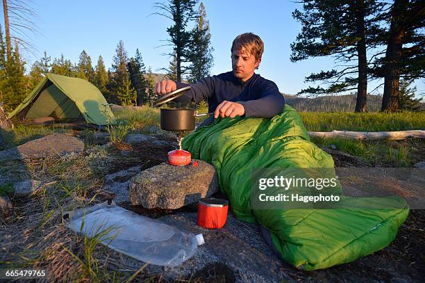 male camper in sleeping bag prepares a meal on camping stove at midnight ridge, colville national forest, washington state, usa - national forest imagens e fotografias de stock