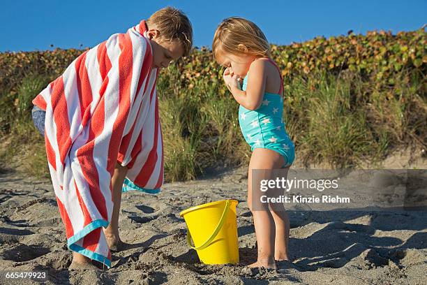 boy wrapped in towel looking down at toy bucket with sister on beach, blowing rocks preserve, jupiter island, florida, usa - striped towel stock pictures, royalty-free photos & images